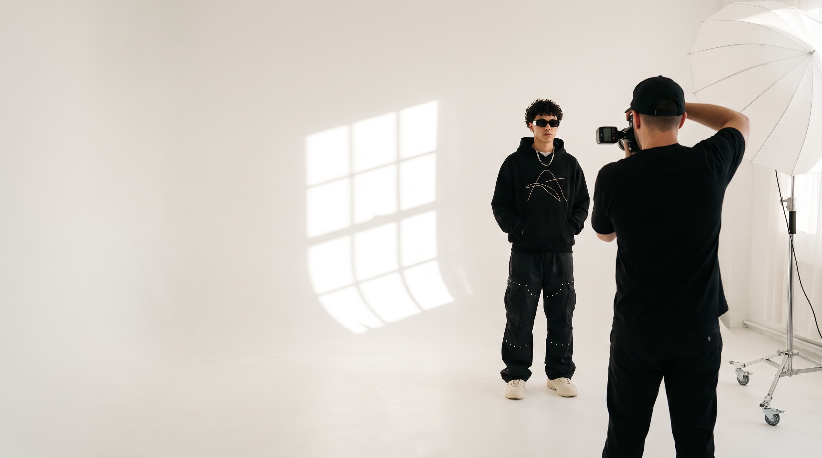 Veyra studio shoot — photographer directing a streetwear model on a white cyc wall