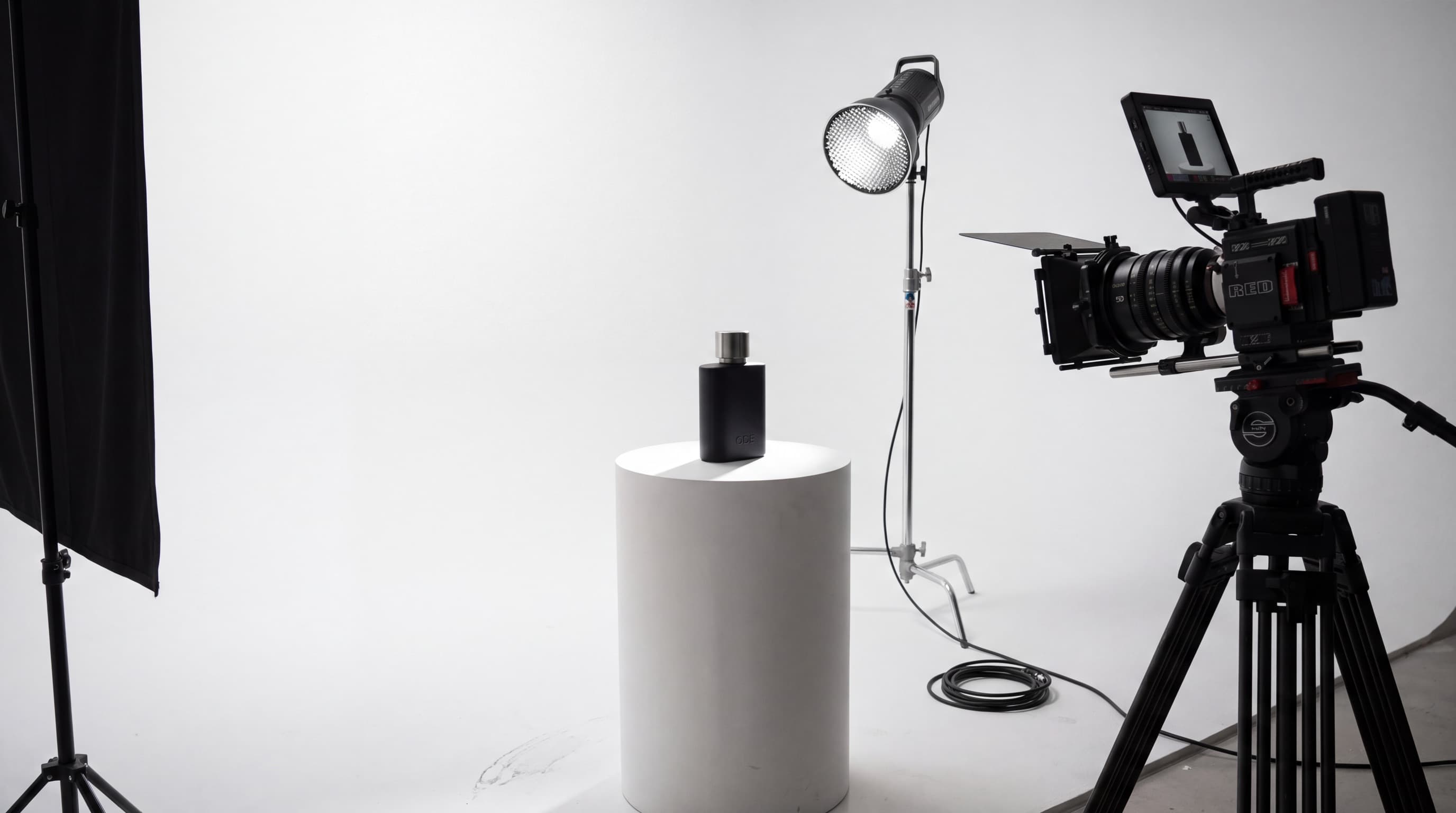 RED Komodo on a tripod in a white studio pointed at an ODE fragrance bottle on a plinth
